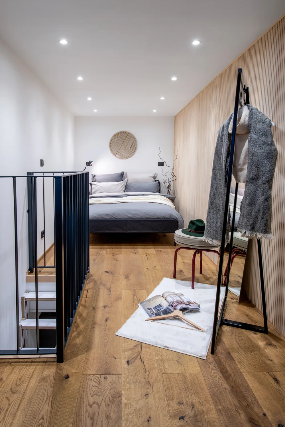 Camera al primo piano con letto, parete in legno e ringhiera nera sopra la scala
