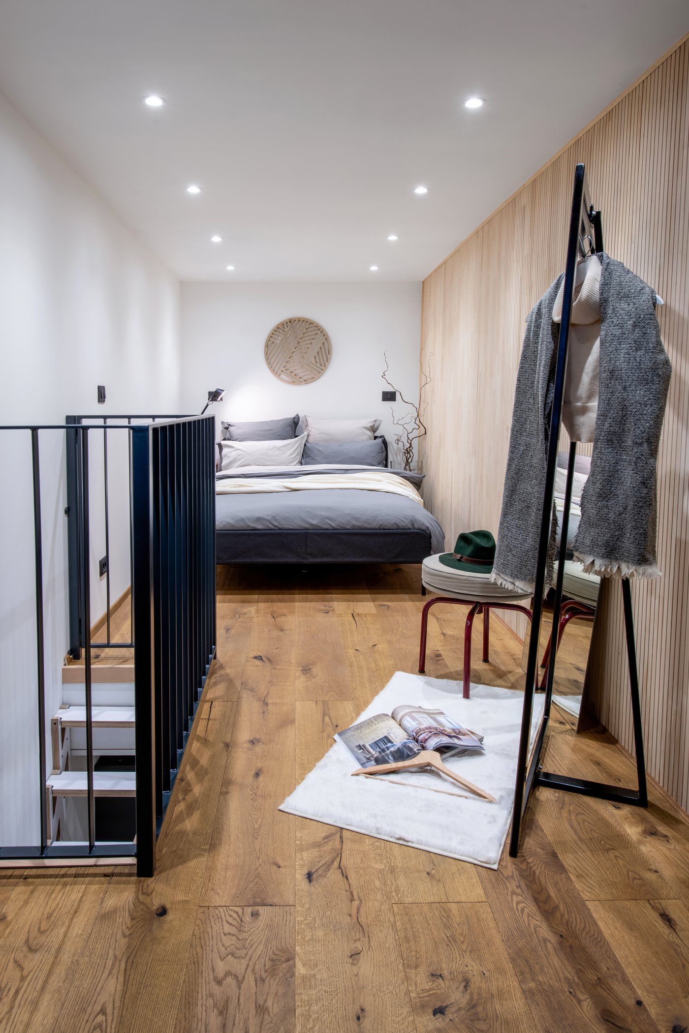 Camera al primo piano con letto, parete in legno e ringhiera nera sopra la scala