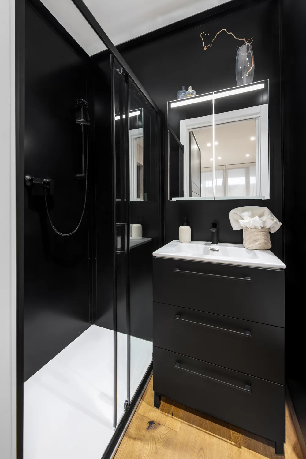 Bagno nero con doccia a tutta altezza, lavabo, mobile e specchio illuminato